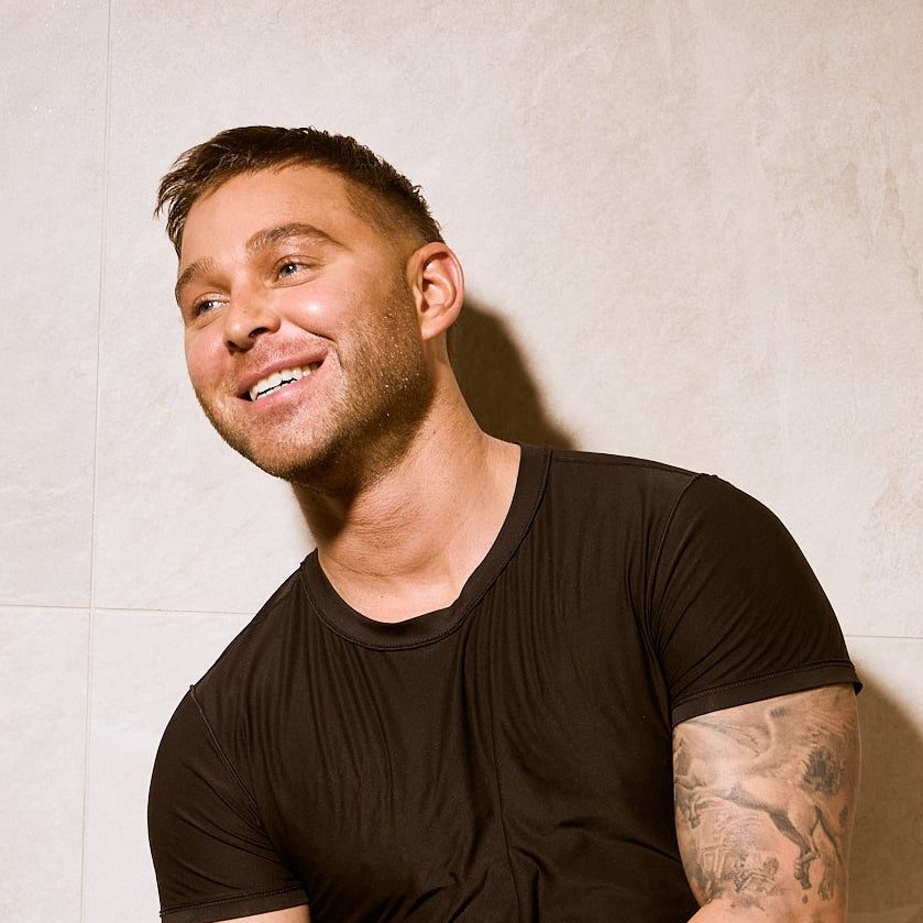 Thomas Tullo, founder of Face Pilates and AMAN Spa, leaning against a light marble wall in the spa.