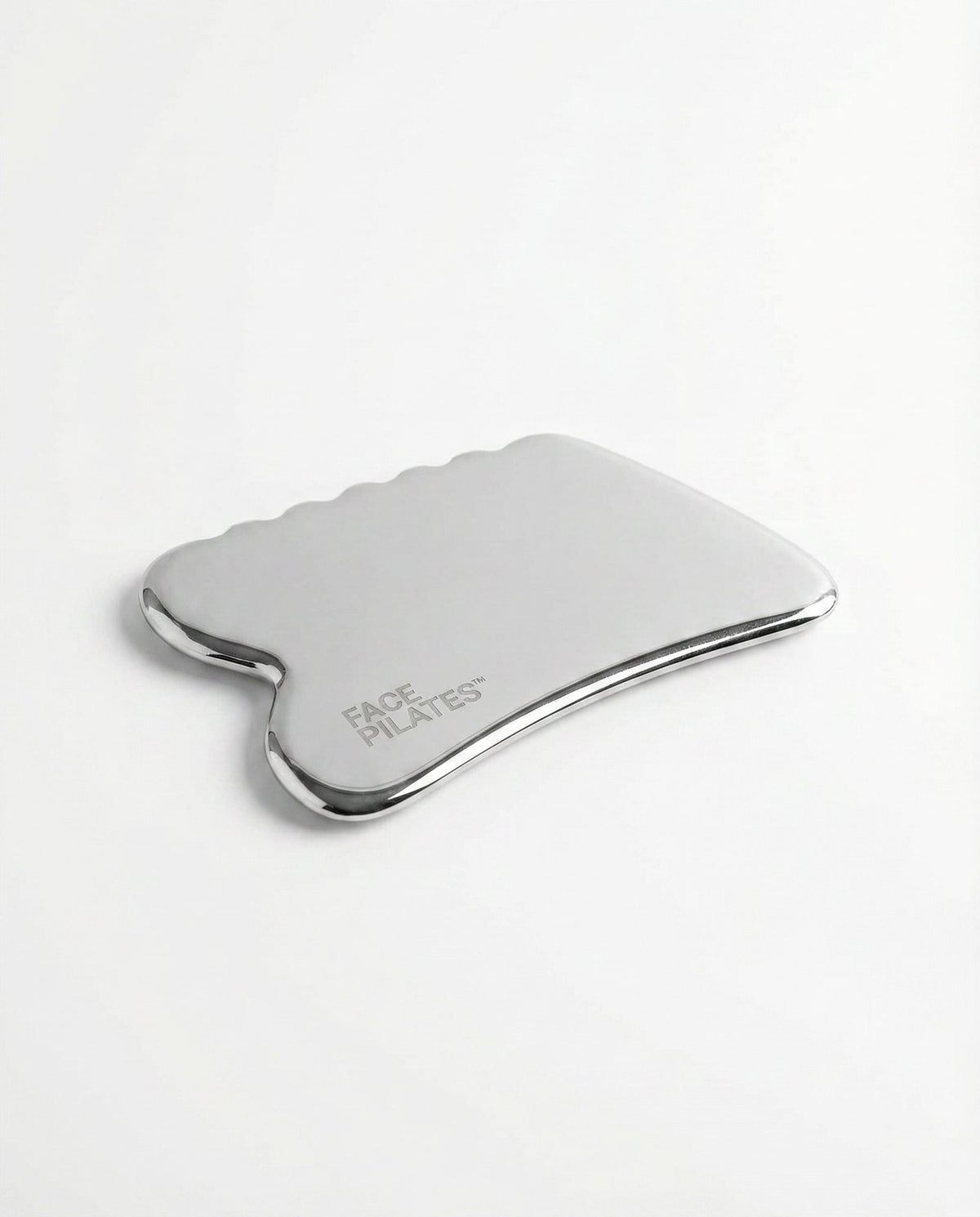A polished stainless steel gua sha massage tool with a curved, scalloped edge and the 'FACE PLATES' logo printed on the side, shown on a clean white background.