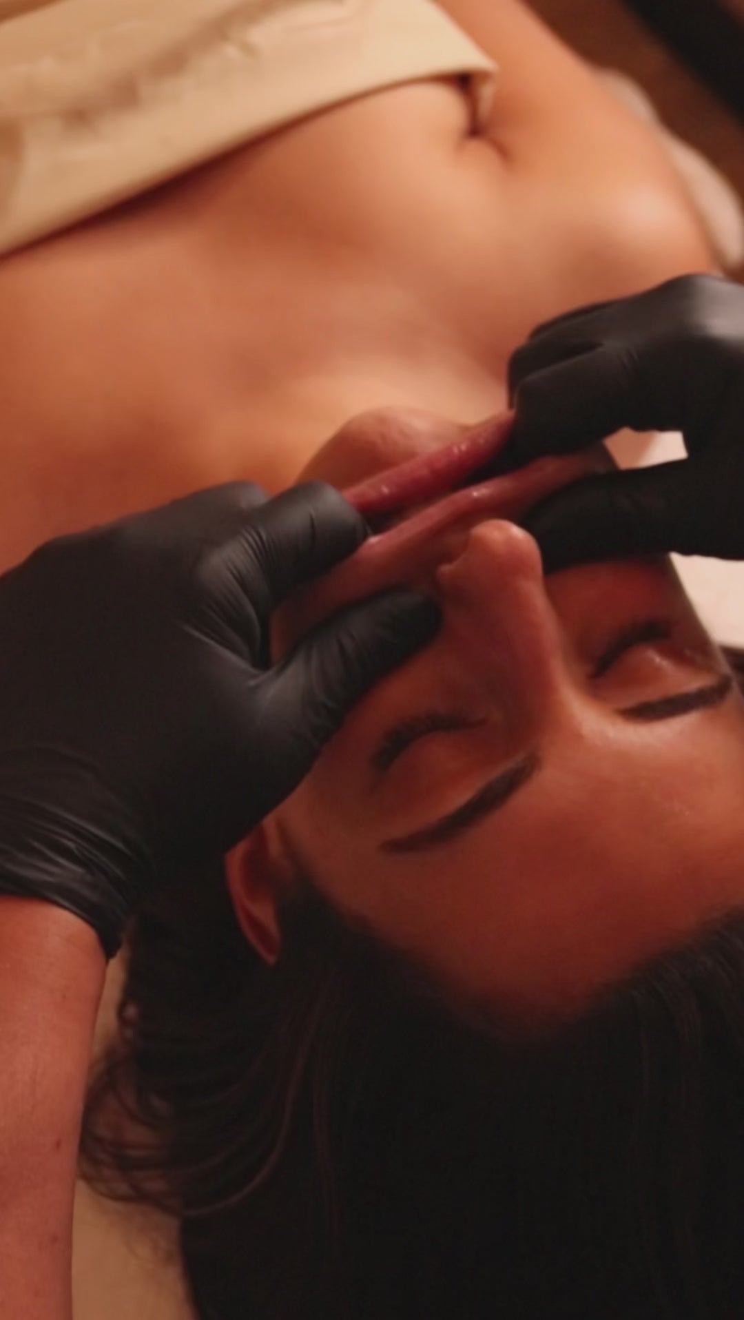 Video showing lip massage as part of a face pilates treatment being performed on a female and the therapist is wearing black medical gloves
